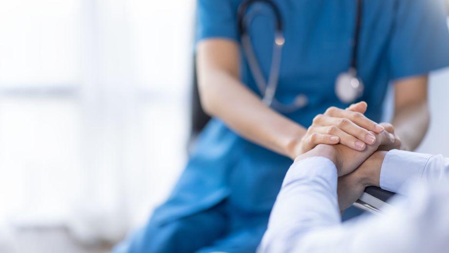 A nurse holds a senior patient's hand. 