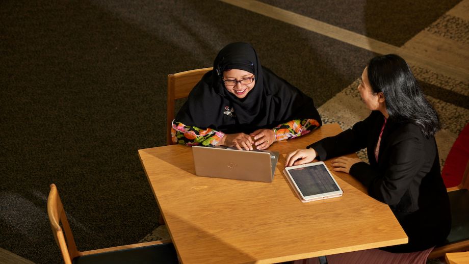 Two women working at a table inside, with the light shining down on them.
