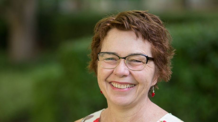 A woman in a garden smiles at the camera.