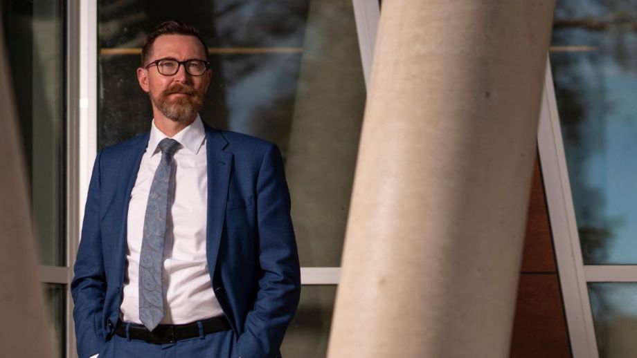 a man standing outside a building, next to a concrete pillar poses for a photo.