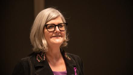 A woman with short, light grey hair and wearing glasses smiles. 