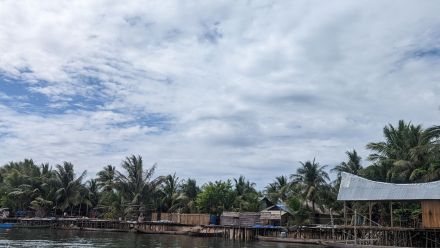 A view of blue, cloudy skies, water and a coastal village in Indonesia. 