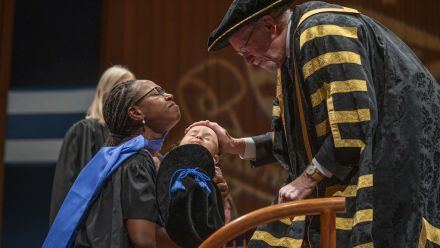 Pictured: a baby carried on stage by a proud mother clad in the PhD regalia of the Australian ýapp University (ANU). This photo, taken at Llewellyn Hall in 2019, features Dr. Veronica Fynn Bruey (PhD '19), a Liberian Canadian, an Indigenous migrant war survivor, an esteemed academic, and a proud mother and feminist.