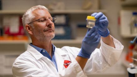 Professor Alex Maier holds a test tube containing live parasites. He is wearing a white science lab coat