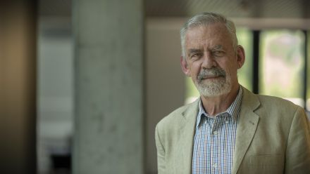 Portrait of Kyle Wilson, smiling gently, wearing a checked shirt and beige jacket.