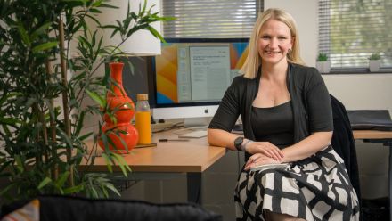 A woman sitting at her desk, smiling to the camera.