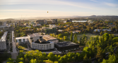 An aerial view of the Australian National University campus, with a hot air balloon the Canberra Civic centre and Lake Burley Griffin in the background. 