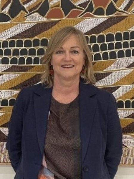 A woman with blonde shoulder length hair stands in front of an artwork.