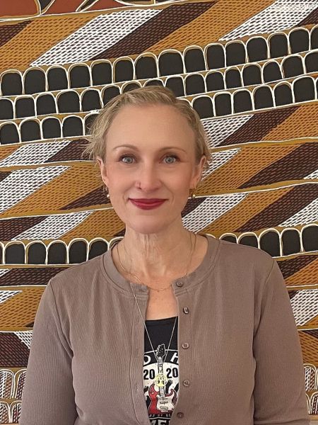 A woman with short blond hair standing in front of an artwork with smile