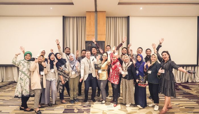 Pictured: ANU Indonesia alumni gathering 2023. Attendees gathered in room smiling and waving arms]