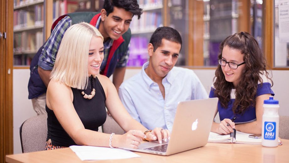 group of students at a table leaning over laptop