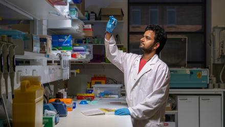 Dr Abhimanu Pandey inspects a test tube containing an unknown substance. He is wearing a white lab coat with a red t-shirt underneath.