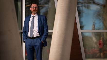 A man wearing a blue suit stands with his hands in his pockets.