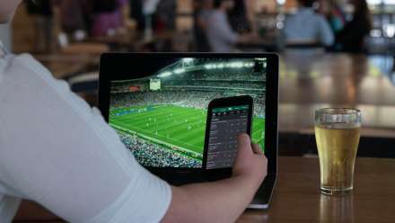 Person holds up their phone while watching a sporting match on their laptop