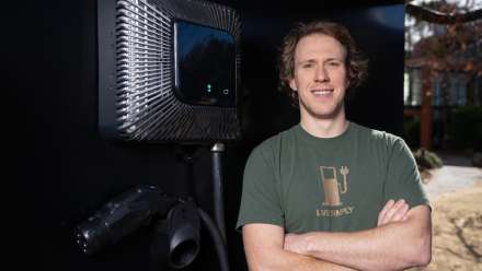 Bjorn leans against an EV charging station with his arms crossed. He's wearing a green t-shirt & smiling.