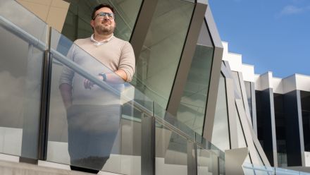 A man leans on a railing outside of a building, looking out.