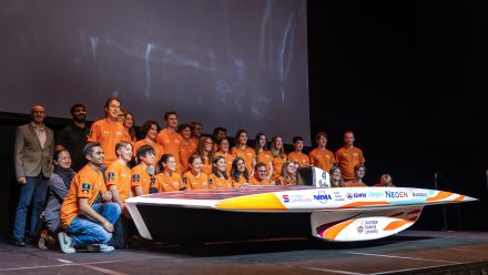 Photo of the solar racing team - all wearing orange shirts - standing behind their new car