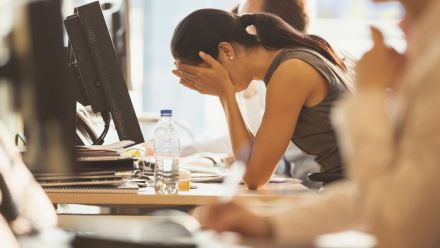 A woman holds her head in her hands at her office desk